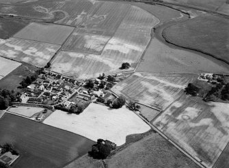 General oblique aerial view centred on the cropmarks of the barrow, enclosures, roundhouses, souterrain, pits and rig at Hatton of Fintray with the village adjacent, looking to the SSE.