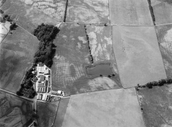 Oblique aerial view centred on the cropmarks of the fort, ring ditch and rig at Mains of Edzell with the farmstead adjacent, looking to the NW.