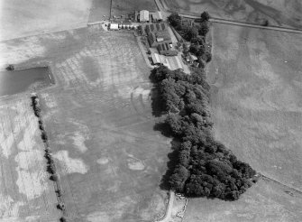 Oblique aerial view centred on the cropmarks of the fort, ring ditch, pits and rig at Mains of Edzell with the farmstead adjacent, looking to the SE.