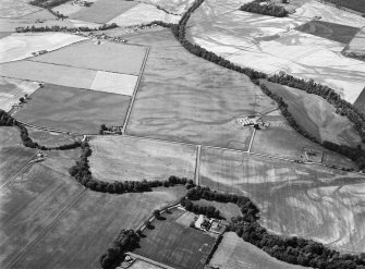 Oblique aerial view centred on the cropmarks of the unenclosed settlement, ring ditches, pits and rig with Stracathro Roman Fort and Temporary Camp adjacent at Smiddyhill, looking to the WNW.