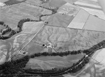 Oblique aerial view centred on the cropmarks of the unenclosed settlement, ring ditches, pits and rig with Stracathro Roman Fort and Temporary Camp adjacent at Smiddyhill, looking to the SSW.