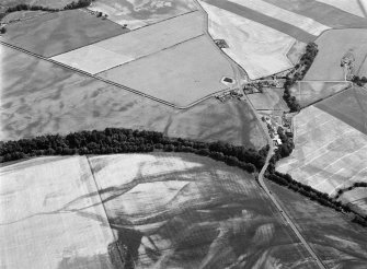 Oblique aerial view centred on the cropmarks of the unenclosed settlement, ring ditches, pits and rig with Stracathro Roman Fort and Temporary Camp adjacent at Smiddyhill and Inchbare, looking to the SSE.
