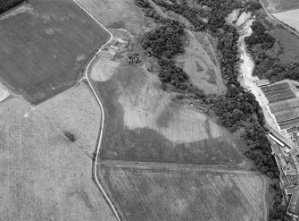 Oblique aerial view centred on the cropmarks of rig, a possible enclosure or long barrow at Rothes with Glenrothes Distillery adjacent, looking to the WNW.
