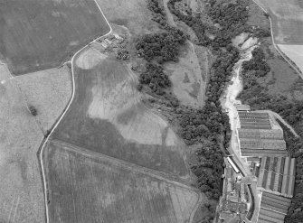 Oblique aerial view centred on the cropmarks of rig, a possible enclosure or long barrow at Rothes with Glenrothes Distillery adjacent, looking to the WNW.
