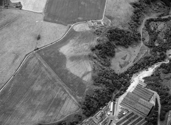 Oblique aerial view centred on the cropmarks of rig, a possible enclosure or long barrow at Rothes with Glenrothes Distillery adjacent, looking to the WSW.

