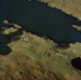 Oblique aerial view centred on the church and burial ground and the remains of the military camp with the hotel and remains of the boat nausts adjacent, taken from the NE.