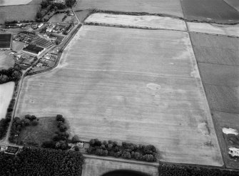 Oblique aerial view centred on the remains of ring ditches at Longmorn with the distillery adjacent, looking to the ENE.