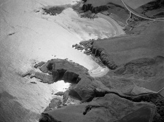 Oblique aerial view centred on the remains of the promontory fort, castle and battery at Cullykhan, looking to the SE.