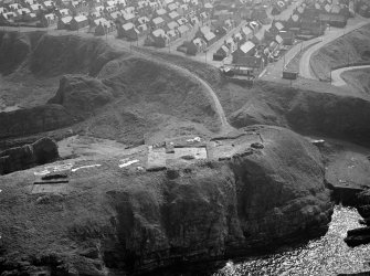 Oblique aerial view centred on the excavation of the promontory fort at Green Castle, Portknockie with the village adjacent, looking to the SSE.