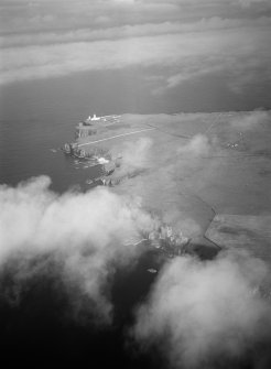 Distant oblique aerial view centred on the remains of Castle Sinclair and Noss Head Lighthouse, looking to the ENE.