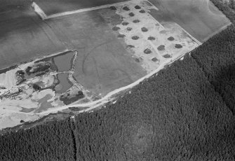 Oblique aerial view centred on the cropmarks of an enclosure, linear features and pits at Dalladies, with the sand and gravel quarry adjacent, looking to the NW.