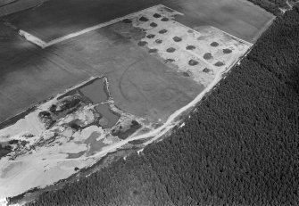 Oblique aerial view centred on the cropmarks of an enclosure, linear features and pits at Dalladies, with the sand and gravel quarry adjacent, looking to the NNW.