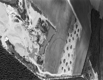 Oblique aerial view centred on the cropmarks of an enclosure, linear features and pits at Dalladies, with the sand and gravel quarry adjacent, looking to the NNE.