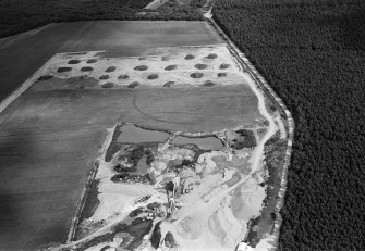 Oblique aerial view centred on the cropmarks of an enclosure, linear features and pits at Dalladies, with the sand and gravel quarry adjacent, looking to the NE.