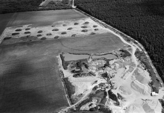 Oblique aerial view centred on the cropmarks of an enclosure, linear features and pits at Dalladies, with the sand and gravel quarry adjacent, looking to the NE.