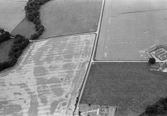 Oblique aerial view centred on the cropmarks of the Roman Temporary Camp at Stracathro with the churchyard adjacent, looking to the SW.