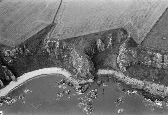 Oblique aerial view centred on the remains of the promontory fort and long cist at West Mains of Ethie, looking to the NW.