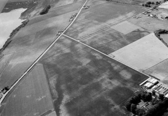 Oblique aerial view centred on the cropmarks of the roundhouses and ring ditches of the unenclosed settlement with the farmstead adjacent at Newbigging, looking to the WSW.