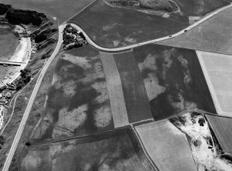 Oblique aerial view centred on the cropmarks of the unenclosed settlement and field system at Braehead with Stonehaven adjacent, looking to the SE.