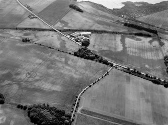 Oblique aerial view centred on the cropmarks of the enclosures, barrow, linear features, pits and rig with the farm adjacent at Gilrivie and Broomley, looking to the SE.