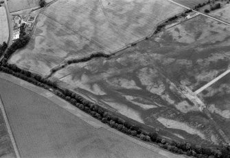Oblique aerial view centred on the cropmarks of the round barrows, unenclosed settlement, souterrains, pits and rig at Auchenreoch, looking to the S.
