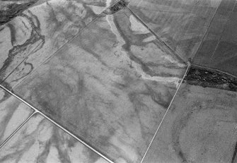 Oblique aerial view centred on the cropmarks of the unenclosed settlement, ring ditches, souterrains and rig at Westside, looking to the SE.