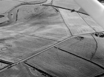 Oblique aerial view centred on the cropmarks of the pit defined cursus and pits at Mill of Fintray with the barrow adjacent, looking to the SW.