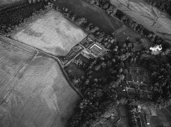 Oblique aerial view centred on the cropmarks of the unenclosed settlement, ring ditches, possible souterrain and pits with Glenbervie House and Policies adjacent at Glenbervie, looking to the SE.