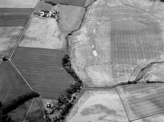 Oblique aerial view of the cropmarks of the enclosure at West Mains of Colliston with the cropmarks at Newton in the foreground, looking to the SSW.