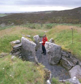 View from N of chamber and passage in chambered cairn; Mrs Angela Gannon (RCAHMS) in picture.
Digital copy of photograph.