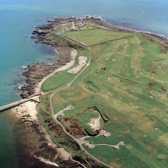 Oblique aerial view centred on the remains of the coastal battery with breakwaters adjacent and lighthouse in the distance, taken from the WNW .