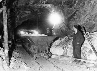 View two mens stood beside waggons transporting silica sand to the surface at the Lochaline mine, Highland.