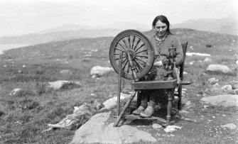 View of Mrs Morrison seated at spinning wheel at Ardhasaig.
