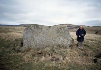 Copy of colour slide (H 93810cs) showing Mr Adam Welfare (RCAHMS) standing beside recumbent stone.