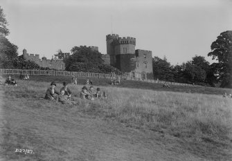 General view of Balloch Castle with people sitting on the bank below.
