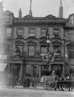 View from south of the bank festooned with flowers and two crowns above each door made of flowers with people outside and horse and cart, possibly for the coronation of Edward VII or George V.