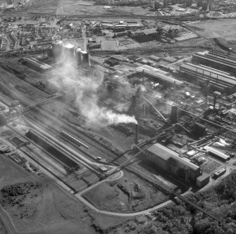 Oblique aerial view. This shows the three cooling towers and two gas holders at the south end of the site (top left), scrap metal preparation area (beyond the coke ovens, with 'white' roof), stripping and mould preparation, casting bay (south) and ladle sevice bay building (top right); coke ovens and blast furnaces (centre)  and blending yard (bottom left). The building on the bottom right is Sinter Plant no. 3 at the north end of the site.