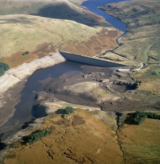 Oblique aerial view centred on the Upper Glendevon Reservoir dam with quarrying associated with its construction, farmsteads, sheepfold and enclosures adjacent, taken during low water from the WSW.