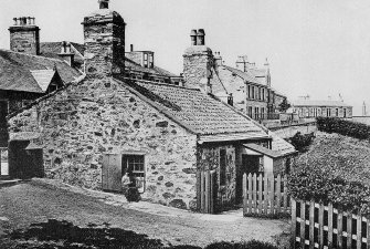 General view of Jeanie Dean's Cottage on edge of Holyrood Park, showing part of St Leonard's Bank behind, and with woman sitting on window ledge of cottage.