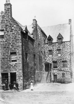 View of houses with family group standing outside.
Titled: 'The Place of Paisley.'
Inscribed on verso; 'In its latter days it became a pub and a low tenement. It is now the Session House of Paisley Abbey. The residence of the Cochranes of Dundonald. Here Jean Cochran was married to John Graham Duke of Claverhouse, "Bloody Claverhouse". He was killed at Killiecrankie. She afterwards married and was killed with her infant son in Holland. Their bodies were discovered in perfect preservation in Kilsyth Old Aisle two hundred years later. See the book "My Lady Dundee" for details.
[Used in Gardner, Alexander "A handbook to Paisley,"and in Rowand, David "Pictorial history of Paisley," (1993) where it is said to have been restored c1912.]