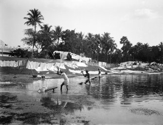 Men washing laundry on a riverbank at a dhobi ghat.  Unknown location.