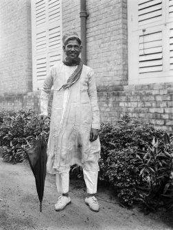 Man, possibly a domestic servant, outside a building.
Unknown location.
