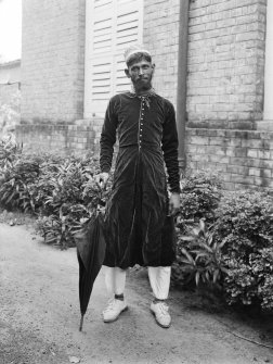 Man, possibly a domestic servant, outside a building.
Unknown location.