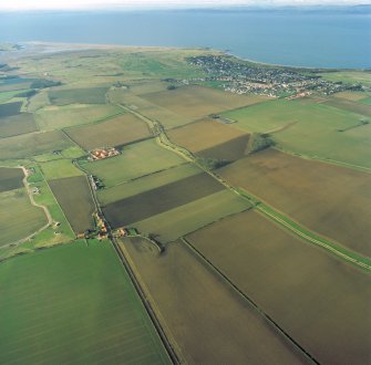 Oblique aerial view looking across the modern amalgamated fields, farmhouse, farmsteading and village towards the golf course and the Firth of Forth, taken from the E.