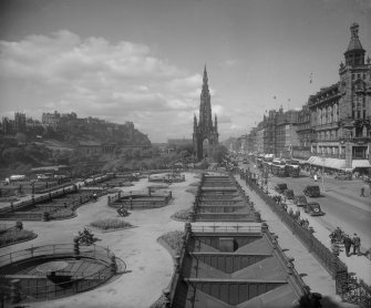 General view of Princes Street looking westwards showing the Castle, Mound, Scott Monument, Waverley Gardens and a busy street with trams, pedestrians and cars