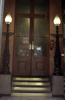 View of cast-iron lamps, one either side of steps leading from foyer to inner door.