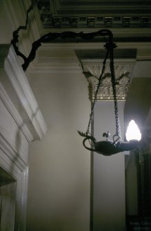 View of hanging lamp, one of a pair hanging from brackets either side of the foot of the stairs.