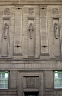 View of part of W facade of National Library of Scotland, showing carved personifications of History, Creative Writing and Law (left to right), with Celtic motif roundels above, and the Royal Arms of Scotland below.