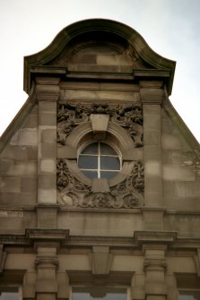 View of carved mask, scrollwork and flowers, around window in gable second from S corner, E side of building (North Bridge).