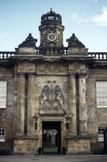 View of entrance to courtyard of Palace, showing crowned cupola, reclining female figures and dolphins; a frieze on which are metopes carved with the cypher of Charles II; and the Royal Arms of Scotland.